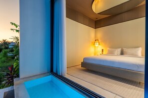 Relax in a serene space with a large bed, bedside table, and a view of lush greenery.
