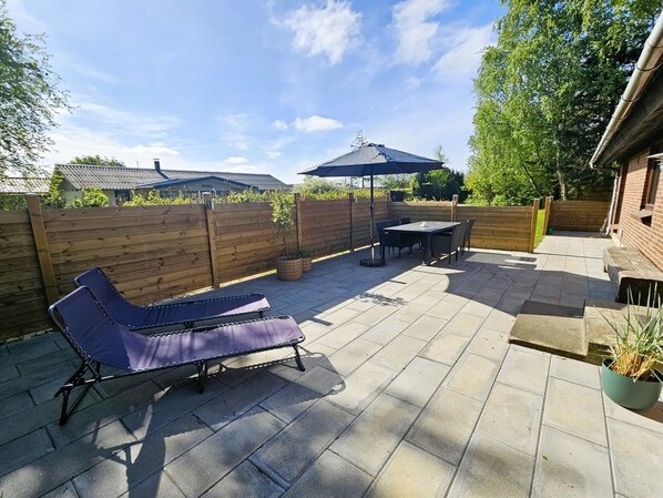 A patio with a table and chairs, a lounge chair, and a wooden fence.
