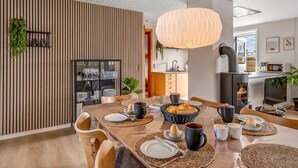 Un espace repas moderne avec un mur à lattes de bois, un grand luminaire suspendu et une cuisine en arrière-plan.