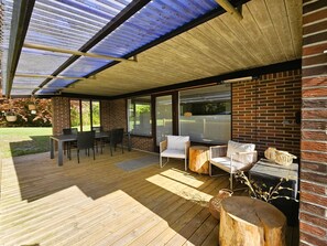 An outdoor patio with a wooden deck, a table with chairs, and a seating area with a sofa and side tables.