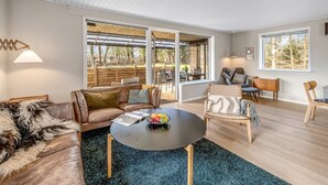 Un salon spacieux avec un canapé en cuir, une table basse ronde et une vue sur l’extérieur grâce à de grandes portes-fenêtres coulissantes.