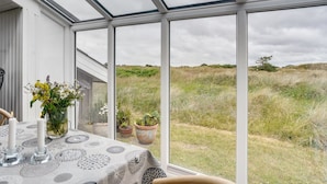 Une véranda avec une table dressée pour le repas, de grandes fenêtres et une vue sur la campagne.