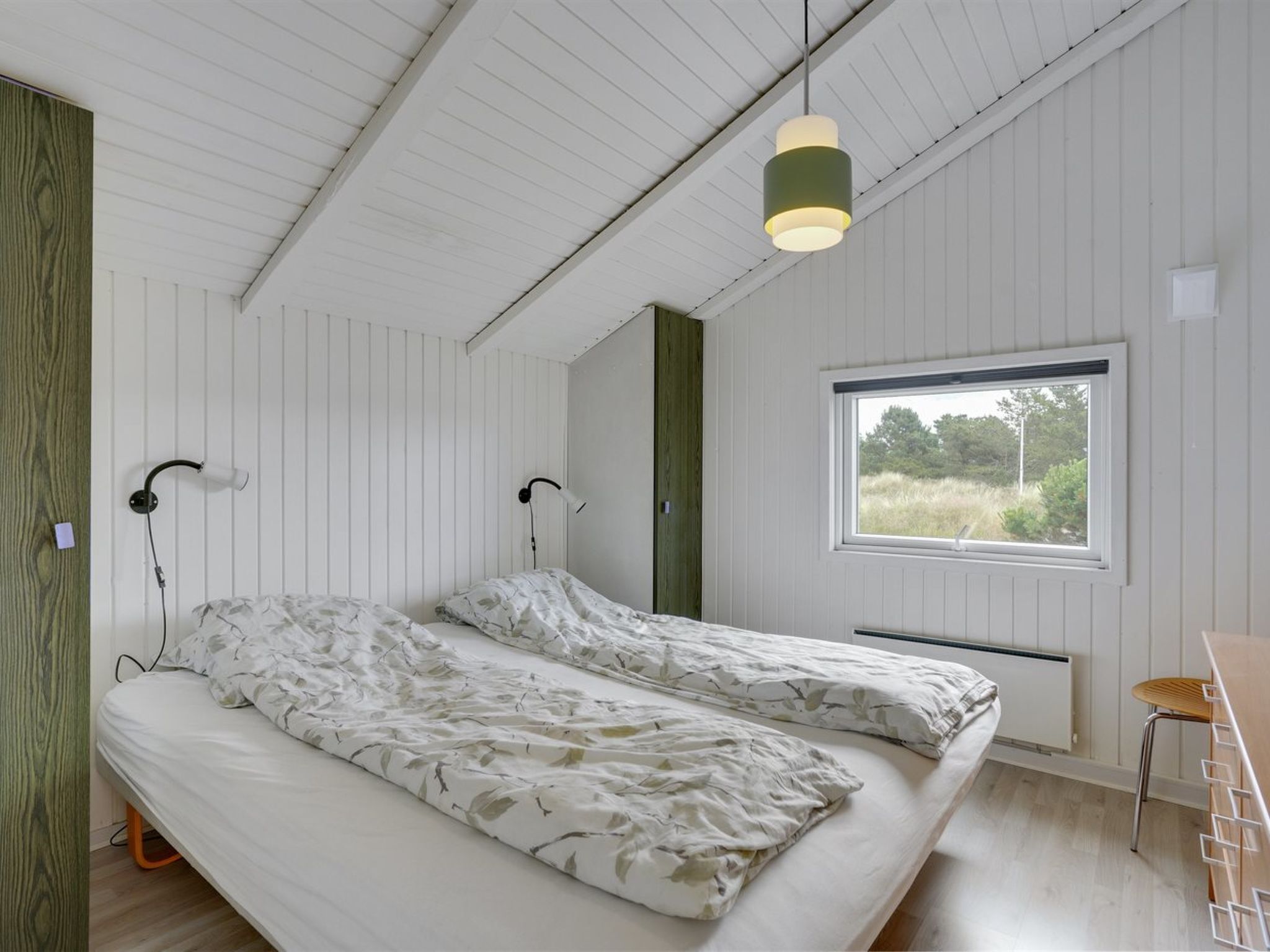 A bedroom with a bed, a window, and a hanging light fixture.