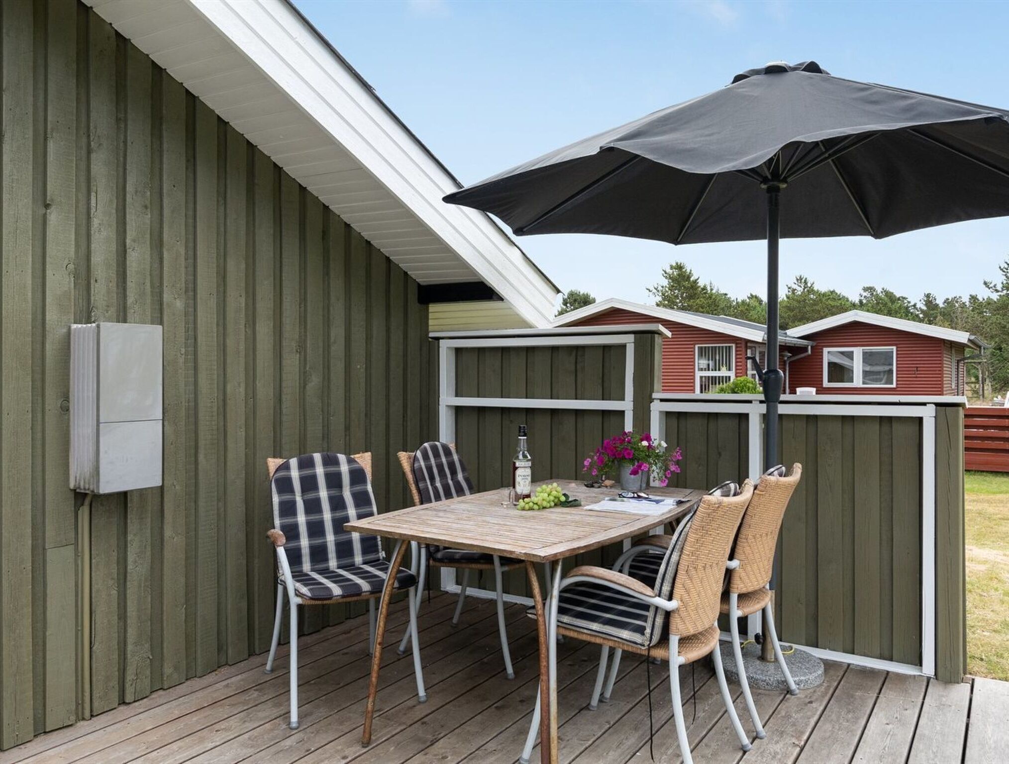 A patio with a table and chairs, a black umbrella, and a wooden deck.