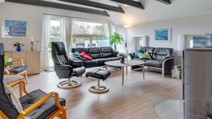Een moderne woonkamer met een zwarte leren bank, een houten salontafel en een glazen eettafel. Een groot raam zorgt voor natuurlijk licht en uitzicht op de omgeving.