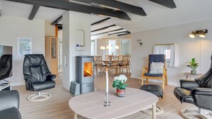 Een moderne woonkamer met een open haard, lederen fauteuils, een eethoek en een groot raam.