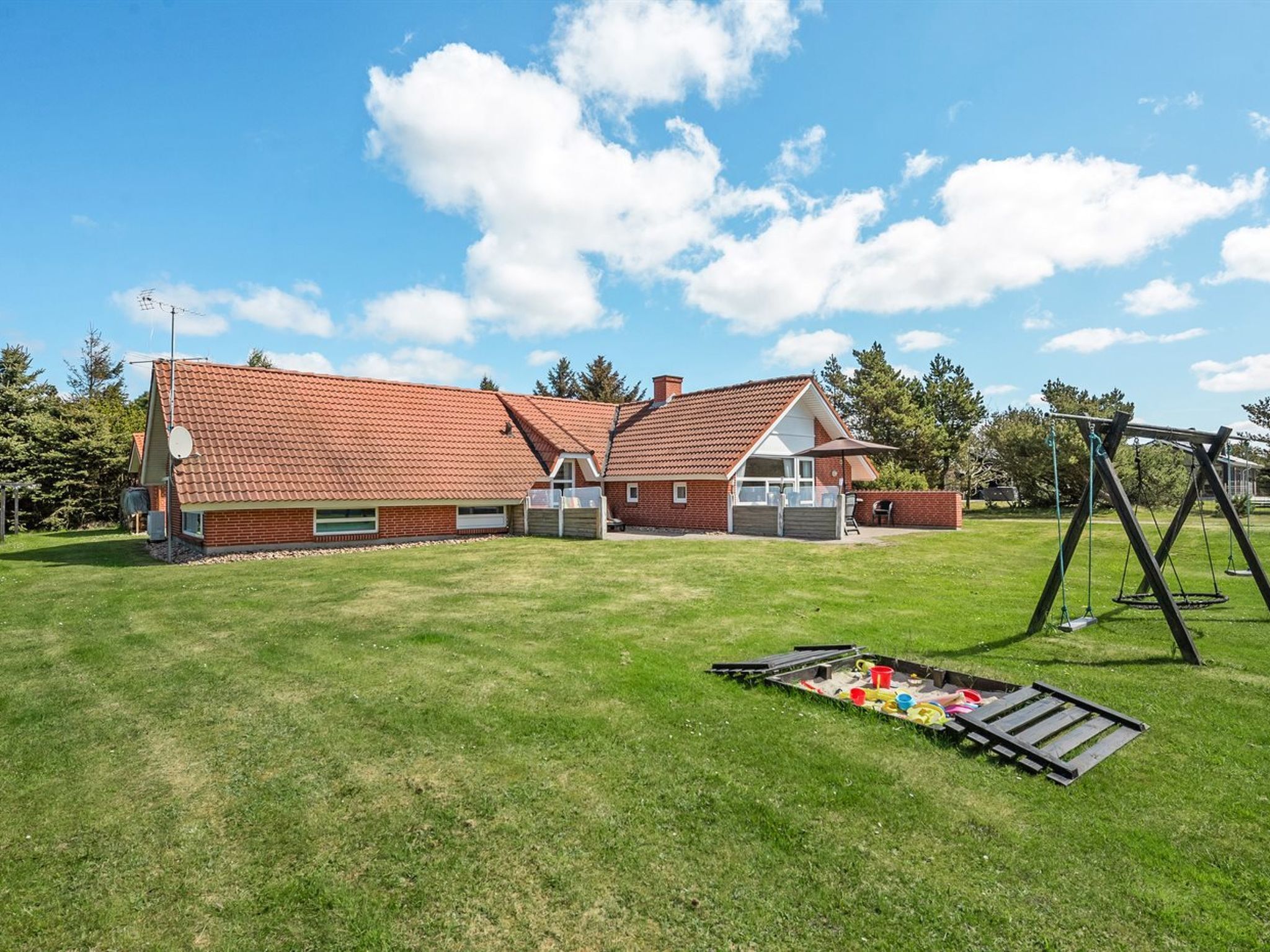 A two-story house with a red-tiled roof, a backyard with a swing set, and a picnic table.