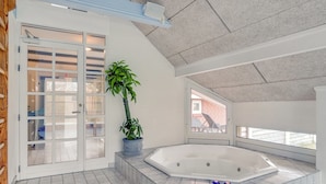 Een ruim zwembad binnen, met een bubbelbad, een plant in pot en een glazen deur naar een buitengebied.