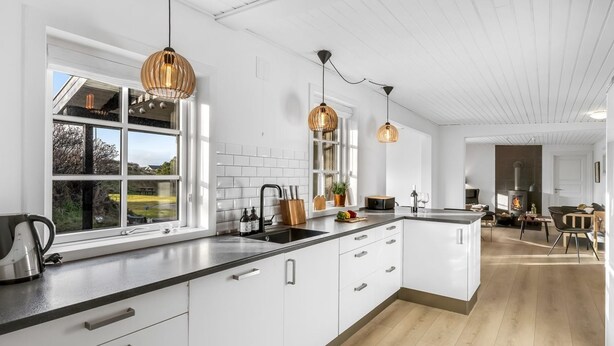 Una cocina moderna con armarios blancos, encimera negra e iluminación colgante.