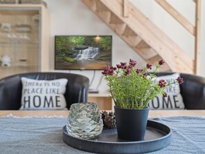 Ein gemütliches Wohnzimmer mit einer Holztreppe, einem Fernseher, der eine Naturansicht zeigt, und einem Blumentopf auf einem Tablett.