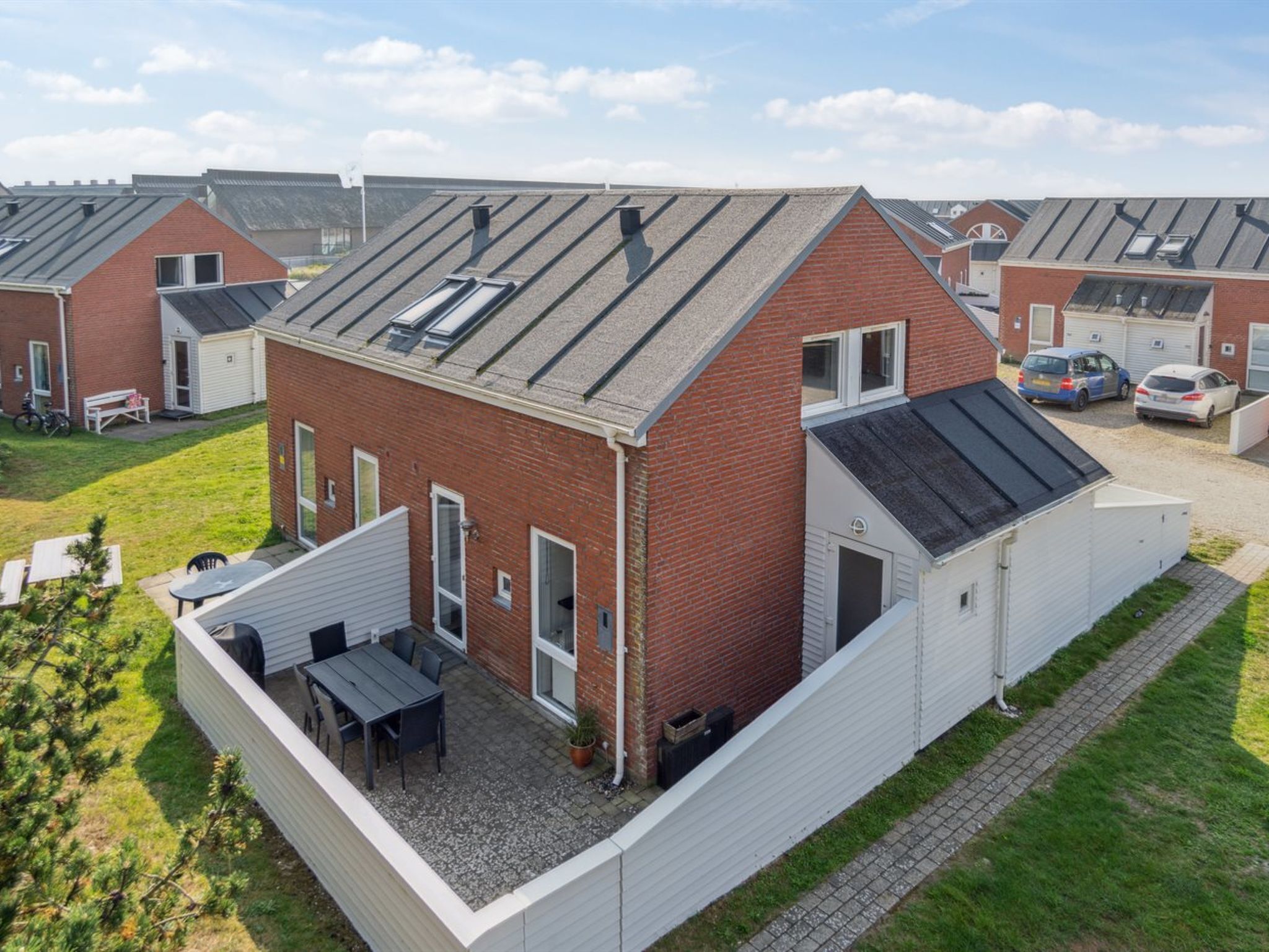 Un immeuble résidentiel moderne doté d’un toit en pente, d’un patio couvert avec mobilier d’extérieur et d’un garage.