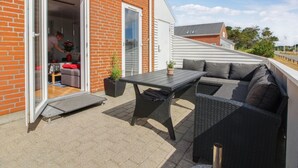 Un patio con mesa y mobiliario exterior, un muro de ladrillo y una puerta corrediza de vidrio que da a un espacio interior.