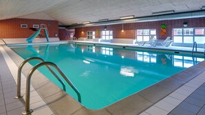 Una piscina interior con tobogán, suelo de baldosas y paredes de ladrillo.