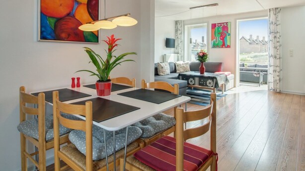 Una sala de estar moderna con comedor, que incluye un cuadro grande, una planta en maceta y un sofá con vistas al exterior.