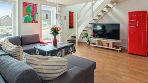 Una sala moderna con un sofá gris, un mueble de televisión rojo y una escalera.