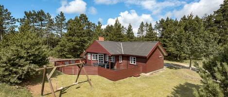 Eine rote Holzhütte mit einer großen Terrasse und einer Schaukel, umgeben von Bäumen und Gras.