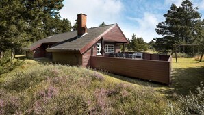 Een chalet met schuin dak, schoorsteen en een omheinde tuin met een schommel.