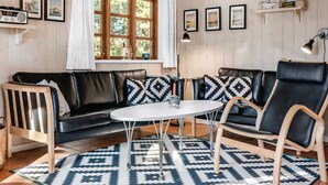 Een gezellige woonkamer met een zwarte leren bank, een ronde witte salontafel en een kamerbreed tapijt met een patroon.