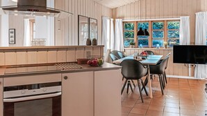 Een moderne keuken met een centraal eiland, een zithoek met televisie en grote ramen voorzien van gordijnen.