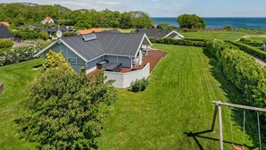 Une propriété résidentielle dotée d’une grande pelouse, d’une terrasse avec mobilier d’extérieur et offrant une vue sur la mer.