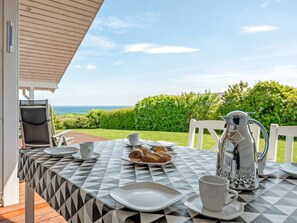 Ein Frühstückstisch mit Meerblick, eine Metall-Kaffeekanne und ein Stuhl.