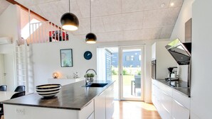 A modern kitchen with a central island, a dining area with a table and chairs, and a staircase leading to an upper level.