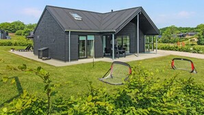 A modern house with a sloped roof, large glass windows, and a patio area.