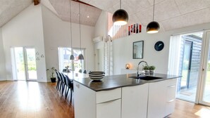 A modern kitchen with a large island, white cabinetry, and a black countertop. There are pendant lights above the island and a clock on the wall.