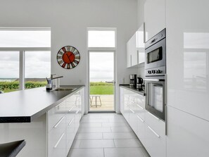 A modern kitchen with a large island, white cabinetry, stainless steel appliances, and a view through large windows. - "Constantin" - 500m from the sea by Interhome (Sjølund)