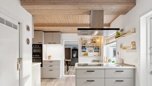 A modern kitchen with white cabinetry, a central island with drawers, a wooden ceiling, and a visible ventilation hood. - "Dana" - 525m from the sea by Interhome (Tranekær)