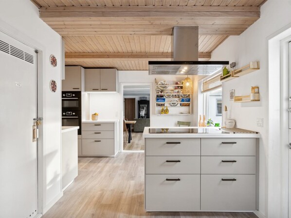 A modern kitchen with white cabinetry, a central island with drawers, a wooden ceiling, and a visible ventilation hood. - "Dana" - 525m from the sea by Interhome (Tranekær)
