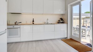 A modern kitchen with white cabinets, a built-in oven, a coffee machine, and a wine bottle on the counter.