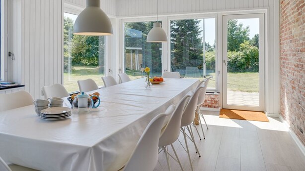 A dining area with a long table, white chairs, and pendant lights.