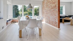 A modern dining area with a long table, white chairs, and a brick wall.