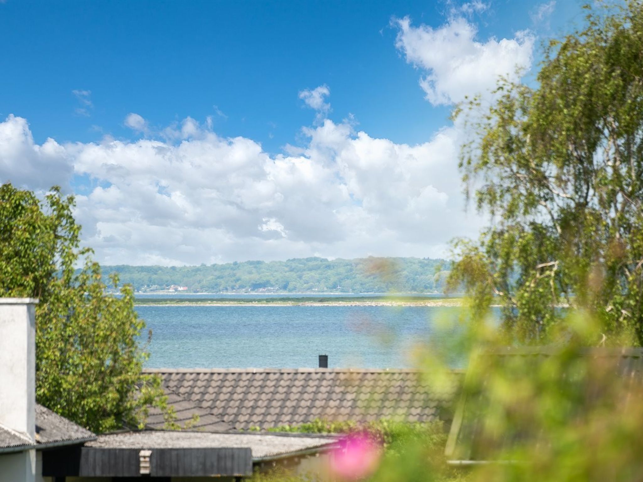 Une vue sur le lac, avec un ciel dégagé, une rive lointaine et un bâtiment surmonté d’un toit en tuiles.
