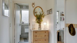 A hallway with a wooden dresser, a mirror, and a vase with flowers. There are two lit candles on the dresser.