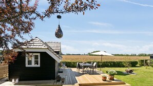 A small wooden house with a deck, a table and chairs, and a garden area with potted plants.