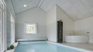 En pool med en bänk, ett badkar och ett fönster med gardiner.