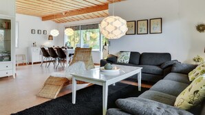 Un salon moderne avec un plafond en bois, un coin repas comprenant des chaises et une table, et un canapé agrémenté de coussins.