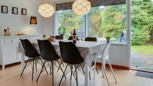 Un espace repas avec un plafond en bois, une table dressée pour quatre personnes et une vue sur la verdure à l’extérieur.