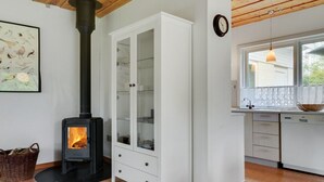 Une cuisine moderne dotée d’un poêle à bois, de meubles blancs et d’une grande fenêtre.