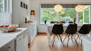 Une cuisine moderne avec un plafond en bois, des meubles blancs et un coin repas avec des chaises noires et une table dressée pour quatre personnes.