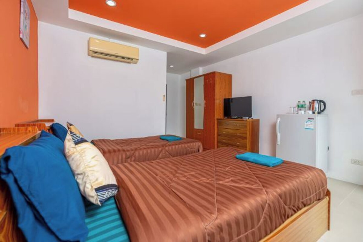 A hotel room with two beds, a wooden wardrobe, a television, and a refrigerator.
