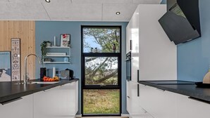 Een moderne keuken met witte kasten, een zwart aanrecht, een spoelbak en een raam met uitzicht op bomen.