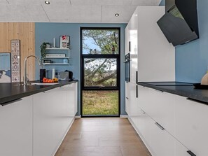 Une cuisine moderne avec des meubles blancs, un plan de travail noir, un évier et une fenêtre donnant sur des arbres.