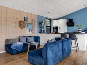 Un salon moderne avec un canapé bleu, une petite table basse et un coin cuisine doté de meubles blancs et d’un plan de travail noir.