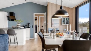 Een moderne keuken met een eethoek, houten details en uitzicht door grote ramen.