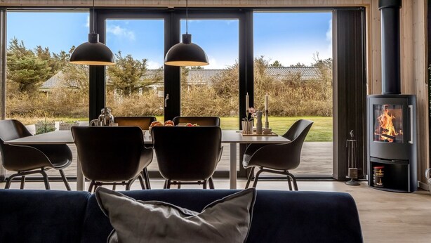 Een moderne woonkamer met een eethoek, grote ramen en een houtkachel.