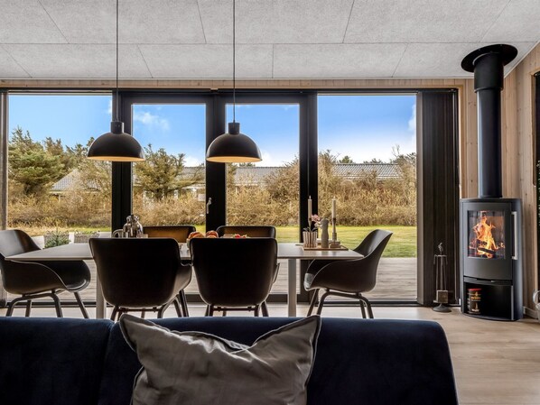 Un salon moderne avec un coin repas, de grandes fenêtres et un poêle à bois.