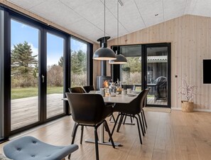 Un espace de salle à manger moderne, doté d’une grande table, de chaises noires et de luminaires suspendus.